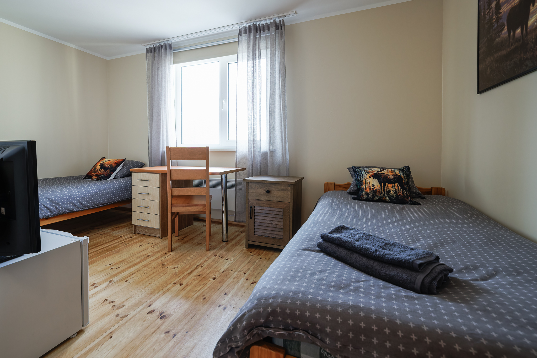 PÕDER tuba Suurlahe Guesthouse majutuses kahe eraldi voodi, puidust põranda, töölaua, tooli, öökapi, rätikute ja suure aknaga.