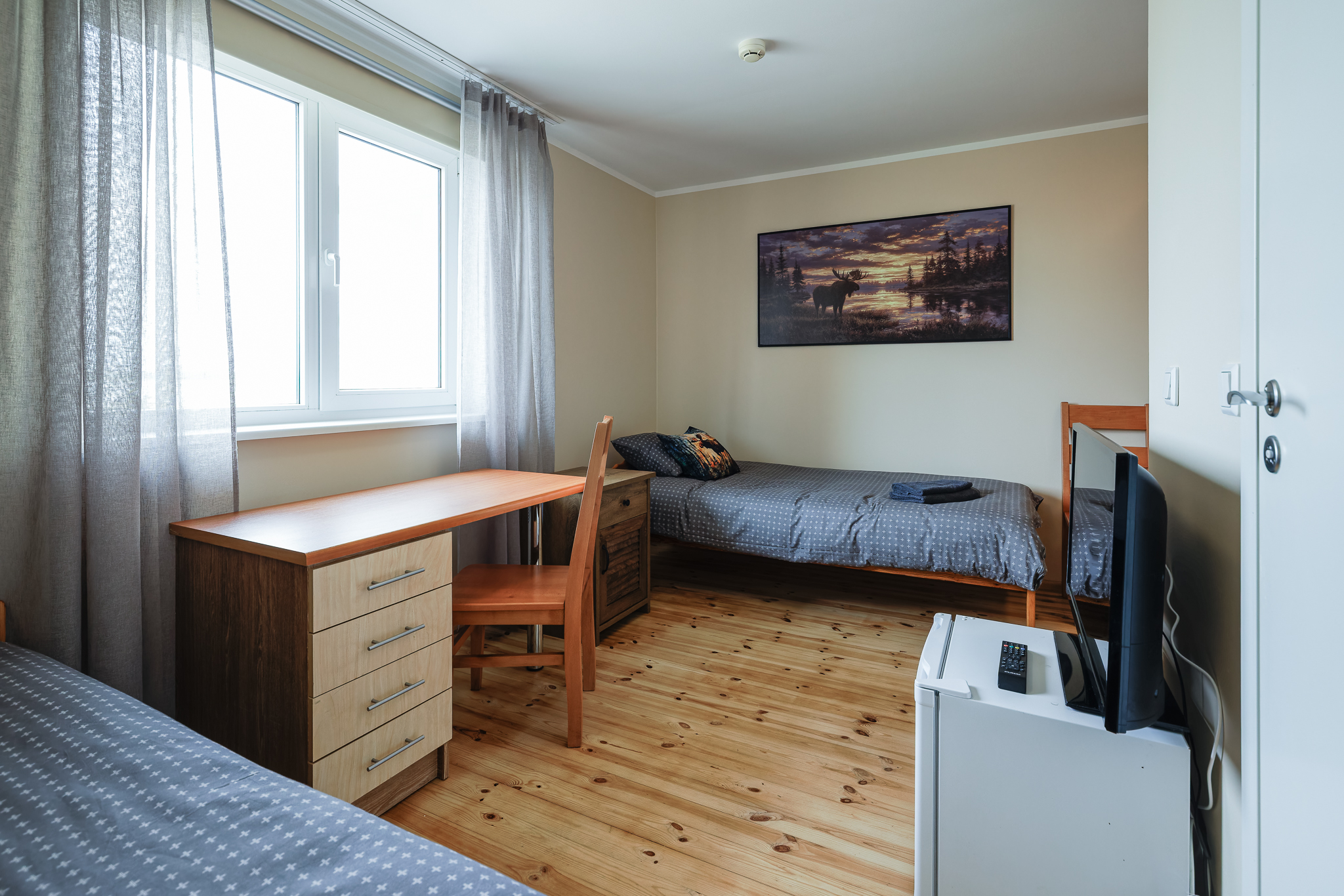 PÕDER tuba Suurlahe Guesthouse majutuses kahe eraldi voodi, puidust põranda, töölaua, tooli, teleri, minikülmiku ja suure aknaga.