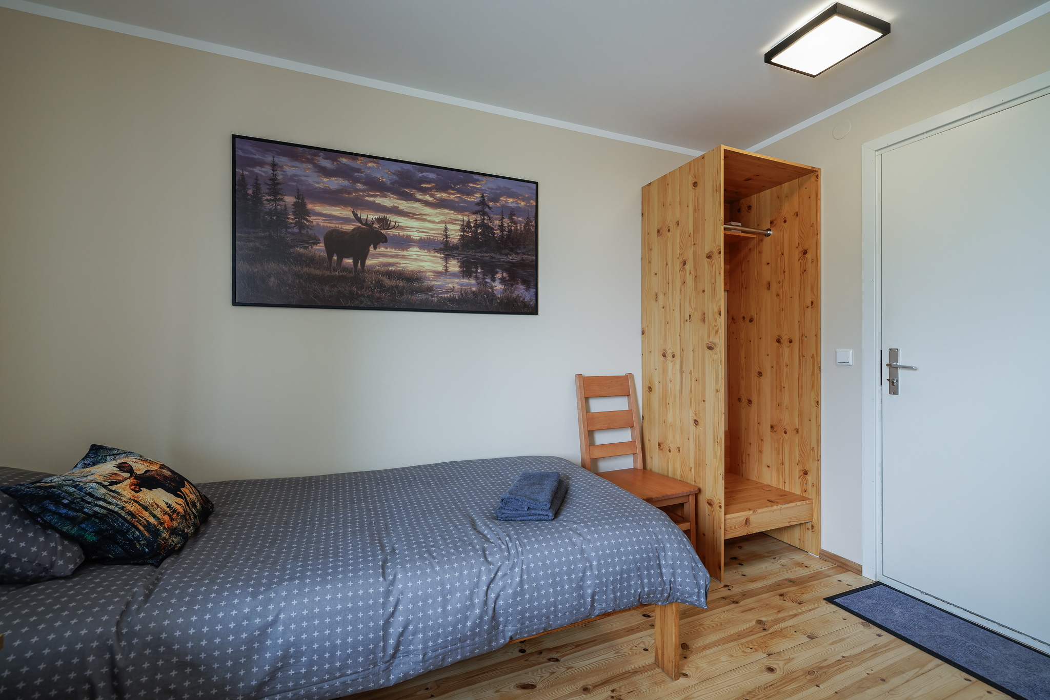 PÕDER tuba Suurlahe Guesthouse majutuses ühe voodi, puidust riidekapi, tooli, puhta rätiku ja põdrateemalise seinapildiga.