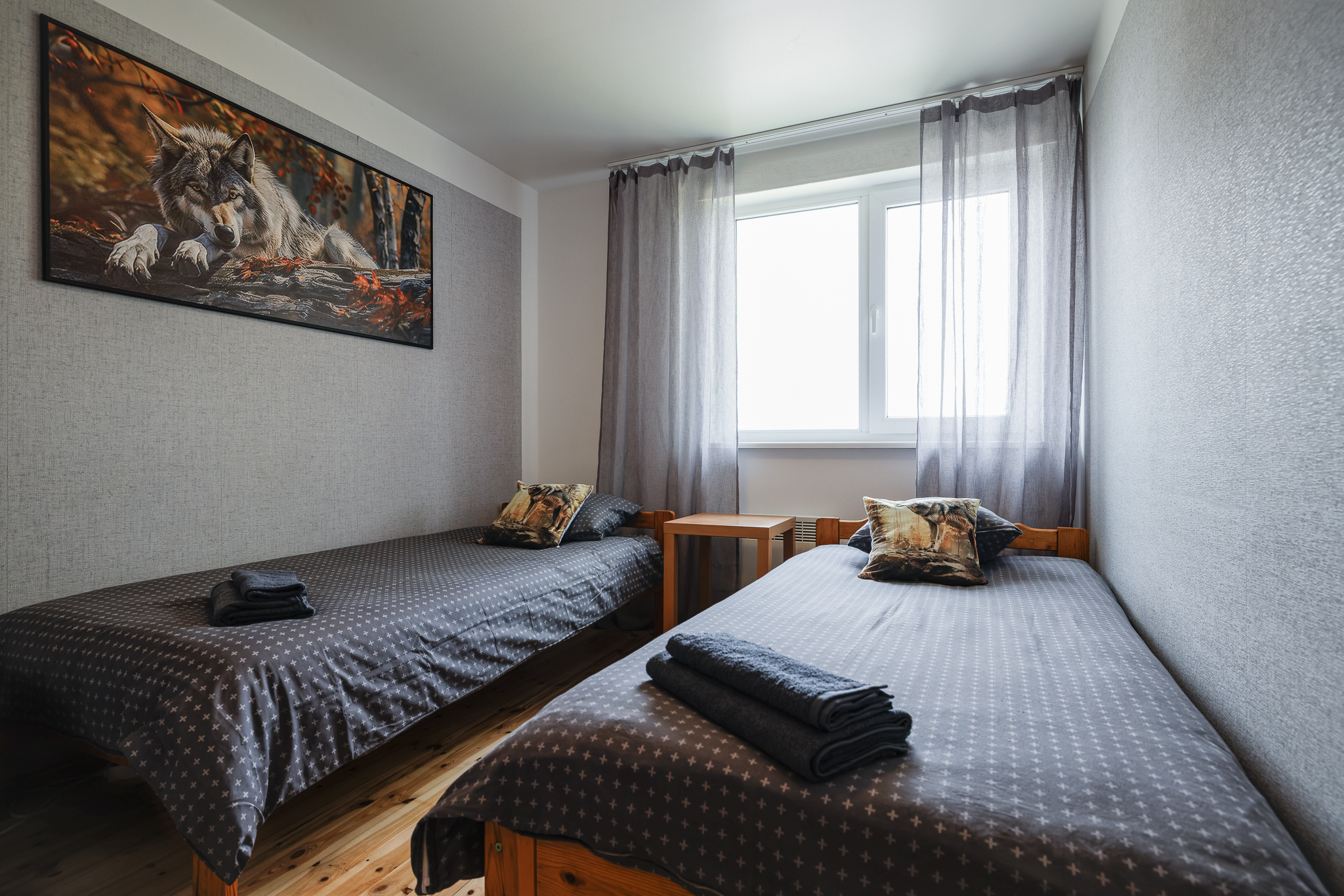 HUNT tuba Suurlahe Guesthouse majutuses kahe eraldi voodi, halli voodipesu, puhaste rätikute, puidust põranda, akna ja hunditeemalise sisekujundusega.