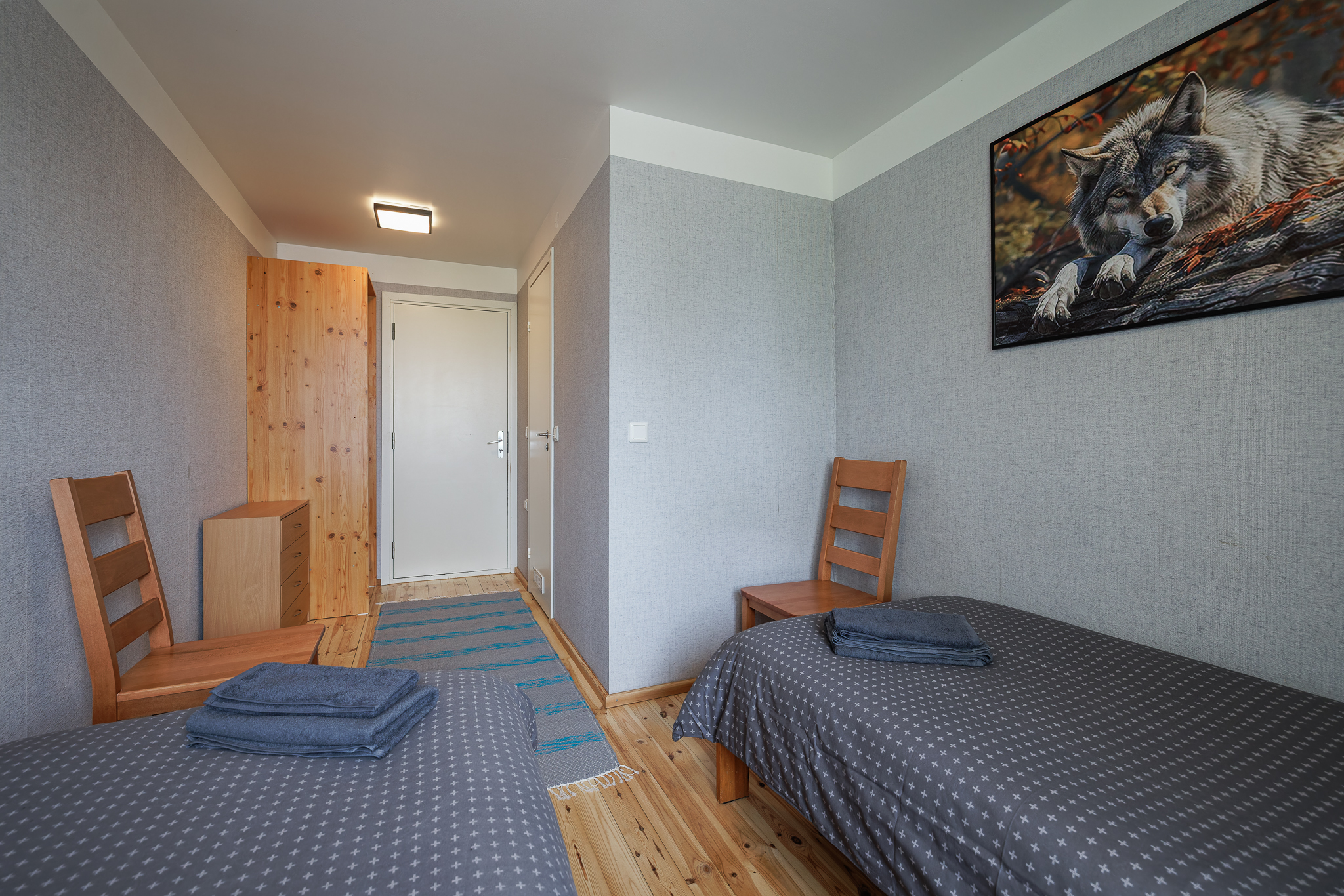 HUNT tuba Suurlahe Guesthouse majutuses kahe eraldi voodi, hallide seinte, puidust põranda, riidekapi, toolide, puhaste rätikute ja hunditeemalise seinapildiga.