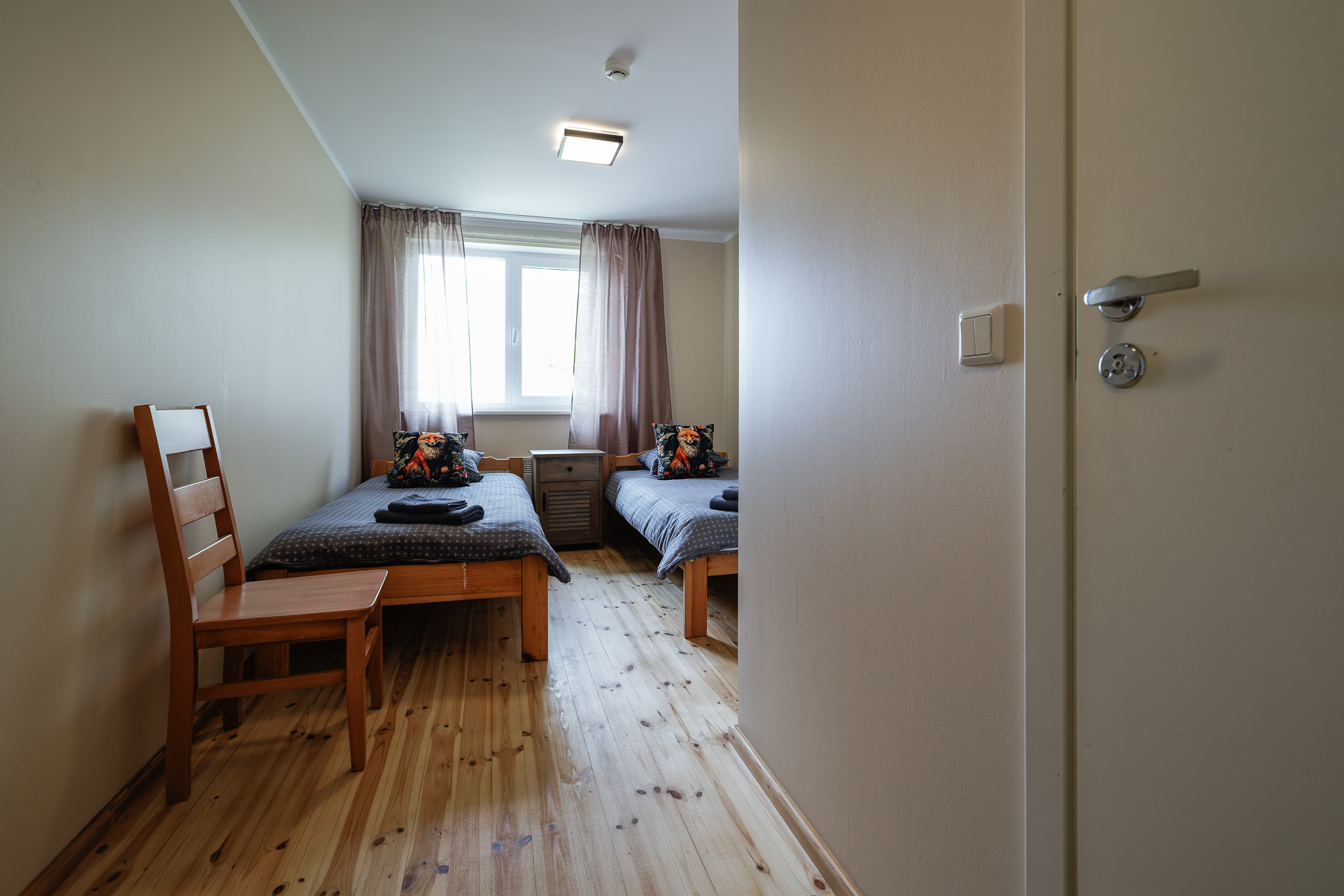 REBANE kaheinimesetuba Suurlahe Guesthouse majutuses kahe eraldi voodi, puidust põranda, öökapi, tooli, akna, puhaste rätikute ja rebaseteemalise seinapildiga.