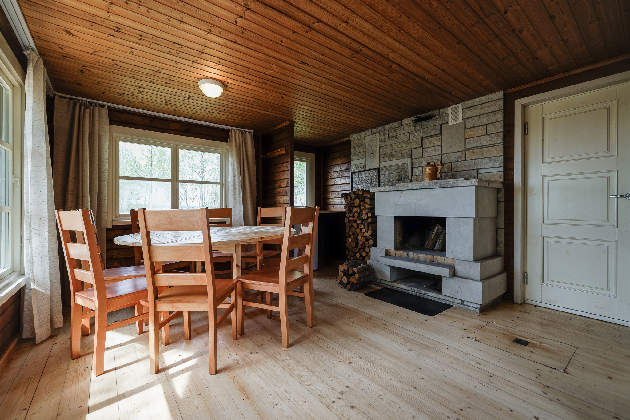 Rustikaalne puidust saunaruum Suurlahe Guesthouse majutuses kamina, ümarlaua, toolide ja loomuliku valgusega.