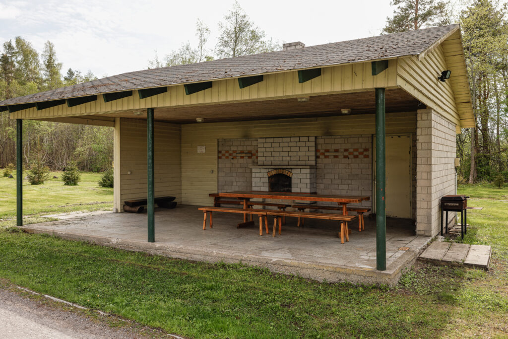 Kaetud väliköögi ja grilliala Suurlahe Guesthouse juures kamina, laudade ja metsalähedase ümbrusega.